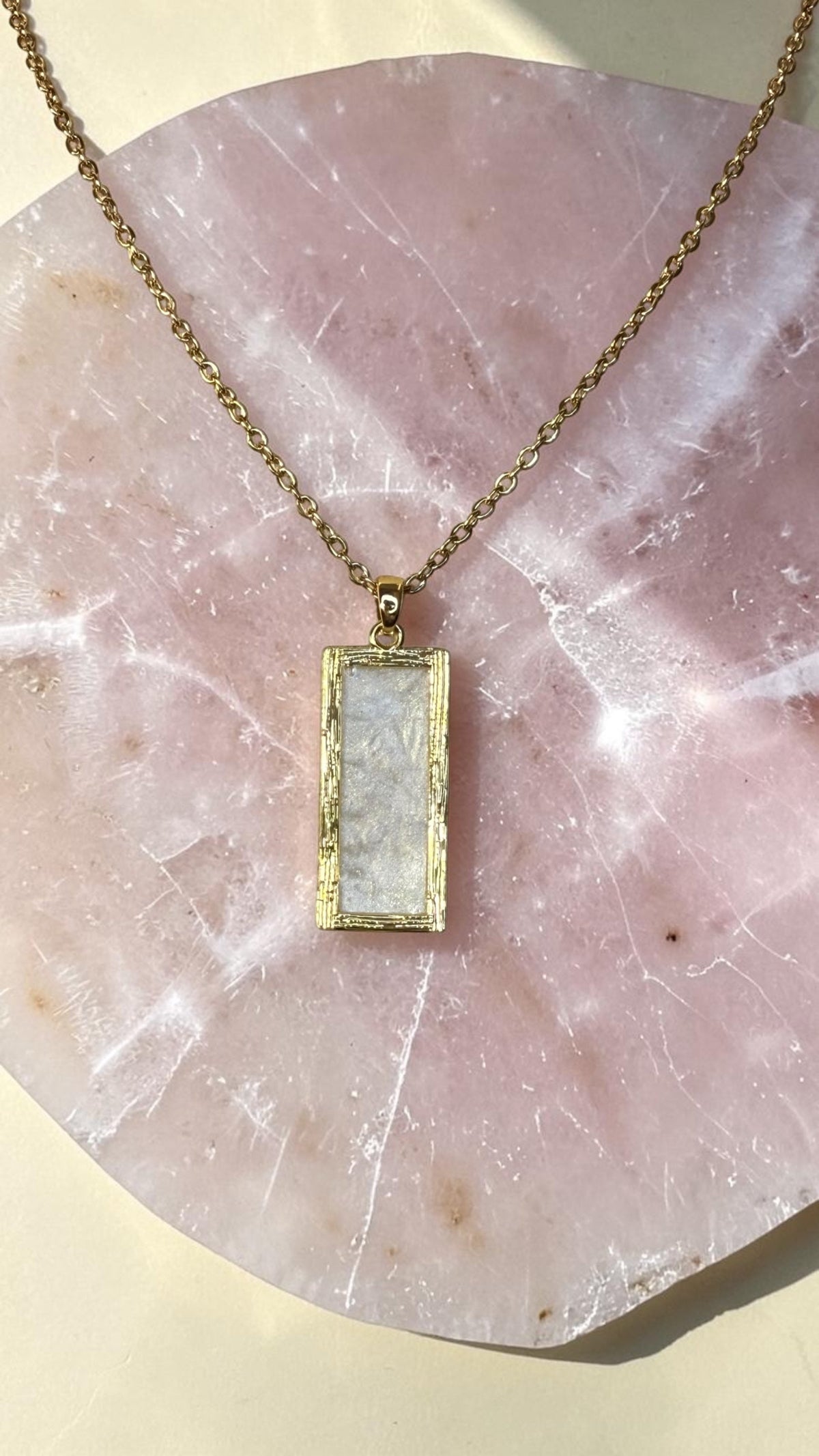 Aurelia Designs handmade rectangular resin necklace with a pearlescent white finish in a gold-toned frame on a stone
