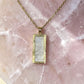 Aurelia Designs handmade rectangular resin necklace with a pearlescent white finish in a gold-toned frame on a stone